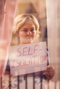 Woman staying in flat in front of window holding a sheet of paper with title self-isolation. People and healthcare concept