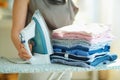 Woman with steam iron, ironing board and ironed clothes