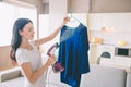 Woman is steaming blue shirt in room. She holds small stream iron in hand. Brunette is concentrated on work. Royalty Free Stock Photo