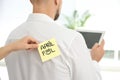 Woman sticking APRIL FOOL note to colleague`s back in office