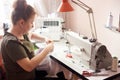 Woman stitching white dress with hands and needle. Sewing machine, scissors, pins, threads, table lamp on background.