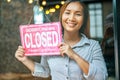 That woman stood holding Closed sign in shop, happily