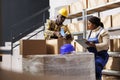 Woman storehouse manager watching warehouse trainee sealing cardboard box Royalty Free Stock Photo