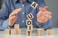 A woman straightens a segment in an unstable tower of cubes labeled Audit