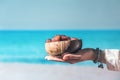 Woman in a straw hat holding in a hand royal dates fruit in a bowl of coconut on a beach with sea view.