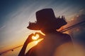 Woman in straw hat making heart symbol with her hands at sunrise near the ocean Royalty Free Stock Photo