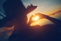 Woman in straw hat making heart symbol with hands at sunset at the ocean Royalty Free Stock Photo