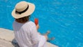 woman in a straw hat relaxes near the swimming pool, drinks a pink cocktail and dangles her legs in the water. Summer Royalty Free Stock Photo