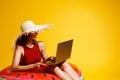 woman in straw hat sits in inflatable ring works on laptop on yellow background. freelance. Travel