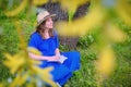 A woman in a straw hat is sitting with a book under a tree. Girl in a blue dress on the grass of a summer park Royalty Free Stock Photo