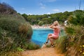 A woman sitting on a cliff, enjoying the picturesque scene of Cala Gat beach in Mallorca
