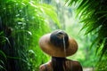 woman with straw hat standing in tropical forest jungle on rainy day. rain season. rear view