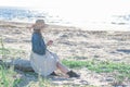 Woman in a straw hat stands by the sea with a glass of wine, rear view