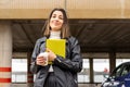 Young woman in jacket holding documents and a coffee in the street