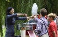 Woman street seller preparing cotton candy for children standing in a line in front of a food moving store