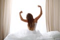 Woman stretching in bed after wake up, back view, entering a day happy and relaxed after good night sleep. Sweet dreams