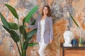 Woman in striped jacked posing in front of big plant. Indoor interior portrait