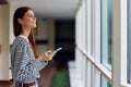 Woman in striped sweatshirt smiling holding phone by the window looking out over the city Royalty Free Stock Photo