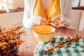 Woman stripping sea buckthorn berries from branches at home and puts it in bowl. Healthy fruit