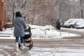 A woman with a stroller and a child goes into heavy snow. Walk with the baby in the pram. Badly cleaned streets of snow, the
