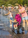 A woman with a stroller at the fountain, a child reaches for the water jets