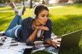 Woman student lies outdoors in a park using laptop computer listening music blowing kisses. Royalty Free Stock Photo