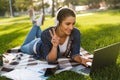 Woman student lies outdoors in a park using laptop computer listening music make peace gesture. Royalty Free Stock Photo