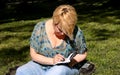 Woman and student sitting on grass, takes notes in notebook, learning and writes thoughts, writes book. Royalty Free Stock Photo