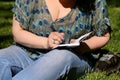 Woman and student sitting on grass, takes notes in notebook, learning and writes thoughts, writes book. Royalty Free Stock Photo