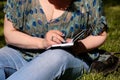 Woman and student sitting on grass, takes notes in notebook, learning and writes thoughts, writes book. Royalty Free Stock Photo