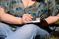 Woman and student sitting on grass, takes notes in notebook, learning and writes thoughts, writes book. Royalty Free Stock Photo