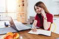 Woman student work on computer while talking on smart phone, use laptop sitting at table in kitchen, freelancer working