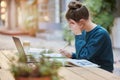 Woman, student and writing in study for elearning, education or working with laptop and books at an outdoor coffee shop Royalty Free Stock Photo