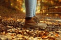 Woman in stylish boots standing on pathway covered with autumn leaves