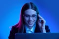 Woman in stylish official suit working on laptop over blue background in neon light. Marketing department Royalty Free Stock Photo