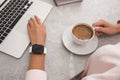 Woman with stylish smart watch and coffee working on laptop at grey table, closeup. Modern device Royalty Free Stock Photo