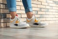 Woman in stylish sneakers near brick wall indoors