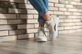 Woman in stylish sneakers near brick wall indoors