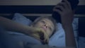 Woman suffering from insomnia uses a smartphone while lying in bed in the dark