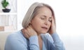 Woman suffering from stress or a headache grimacing in pain as she holds the back of her neck with her other hand to her Royalty Free Stock Photo