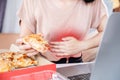 woman sufferings from stomachache after overeating junk food pizza at the office desk hand holding her stomac Royalty Free Stock Photo