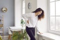 Woman with lumbago pain standing by the window sill and holding her hand on her lower back