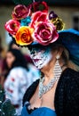 Woman with sugar skull makeup and mexican traditional paper flowers headdress attends dia de los muertos celebration