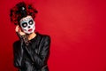 Woman with sugar skull makeup, wreath of flowers on her head and skull and black gloves looks surprised at the free space on the