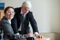 A woman in a suit signs documents under the direction of a mature male boss. Friendly colleagues talking in the office