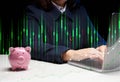 A woman in a suit sits at a table and works on a laptop, next to it is a ceramic piggy bank. Business indicators growth concept, Royalty Free Stock Photo