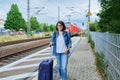 Woman with suitcase backpack on outdoor platform of railway station