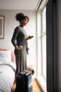 Woman With Suitcase Checking Out Of Boutique Hotel Waiting For Taxi Ordered On Mobile Phone App Royalty Free Stock Photo