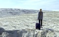 Woman with suitcase with his head down in office wear walking toward infinity in desert place