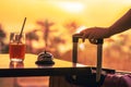 Woman with suitcase ringing hotel service bell with welcome drink and sea and palm tree view on sunset. Travel concept. 24-hour